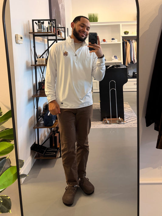 A man takes a mirror selfie in a boutique showing a white long-sleeve quarter-zip shirt with a small LSU Vintage Tiger embroidered logo on the left chest, paired with brown pants and brown shoes.